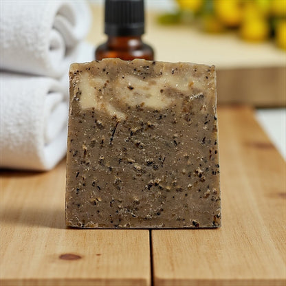 Bar of coffee vanilla tallow soap with visible ingredients on a wooden surface, with a towel and essential oil bottle in the background.