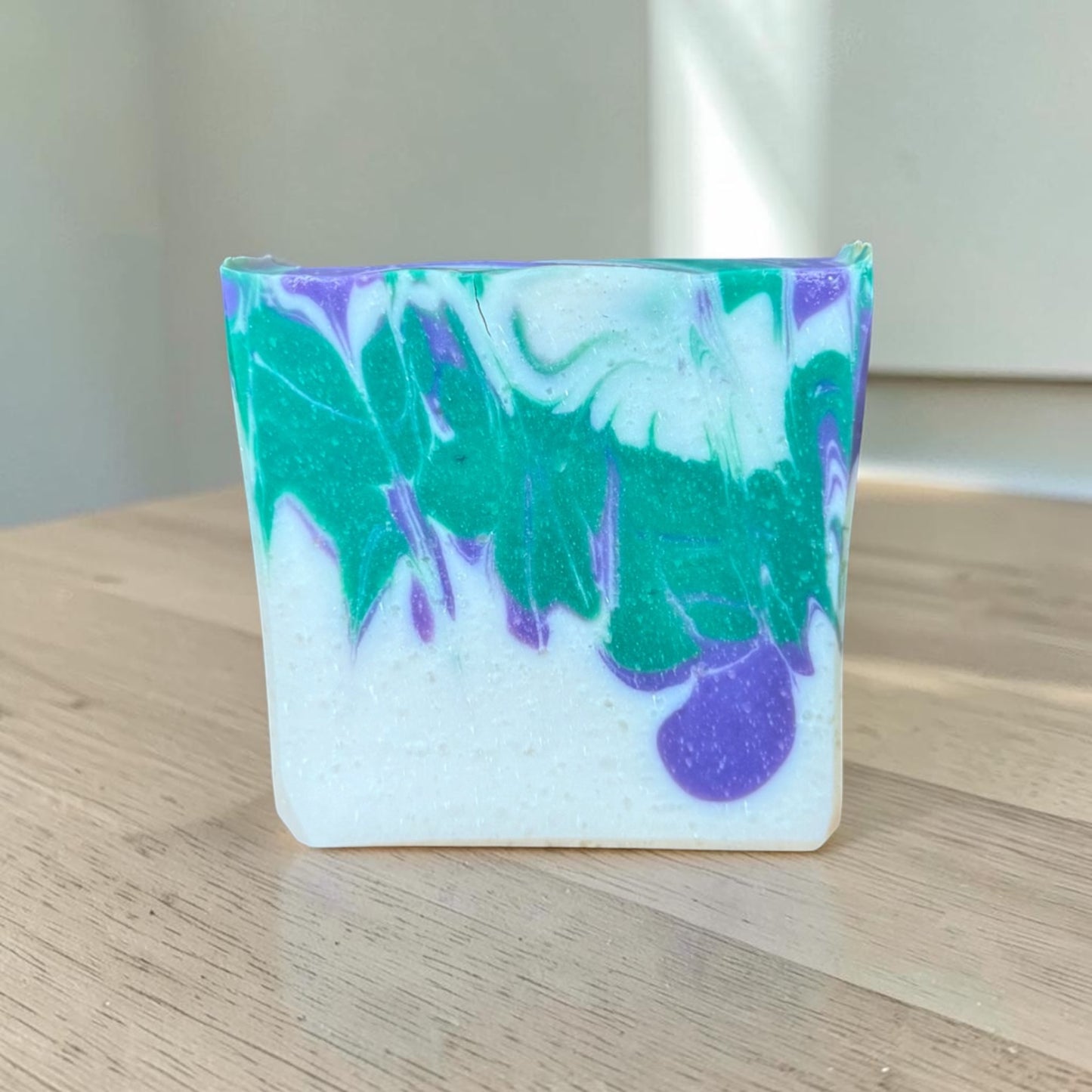Marbled soap bar with green, purple, and white colors on a wooden surface.