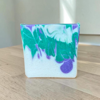 Marbled soap bar with green, purple, and white colors on a wooden surface.