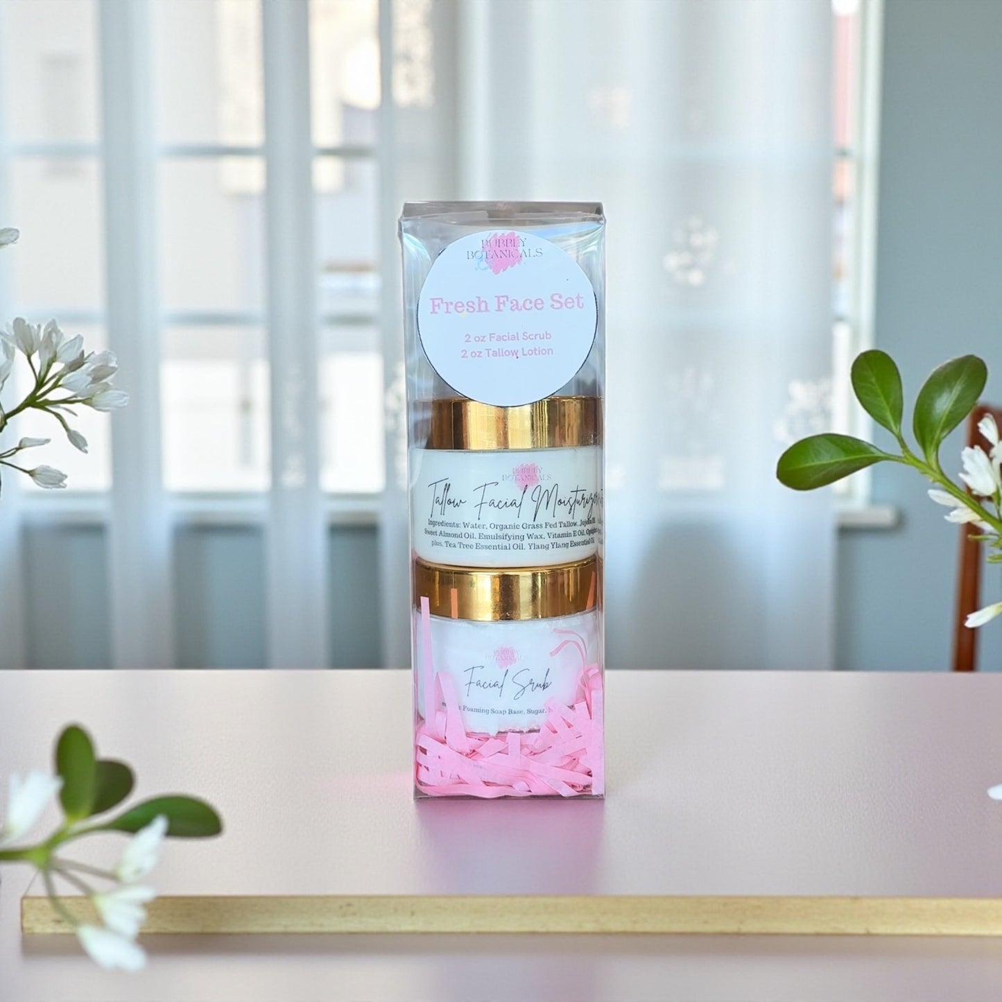 Facial care set with gold and pink packaging on a white surface with plants in the background