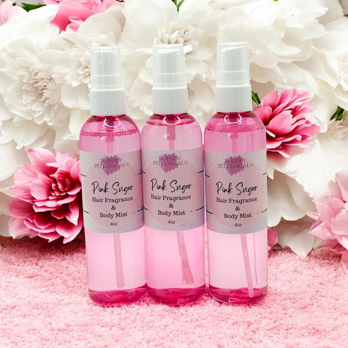 Three bottles of Pink Sugar hair fragrance and body mist with flowers in the background