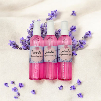 Three pink bottles of lavender magnesium spray with lavender flowers on a beige background