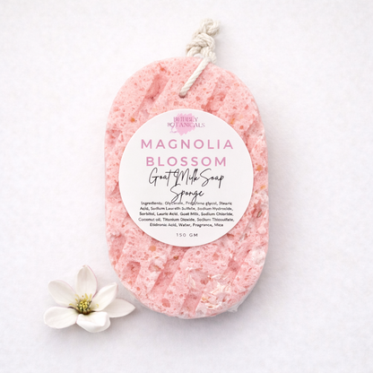 Pink magnolia blossom scented goat milk soap sponge with a label on a white background