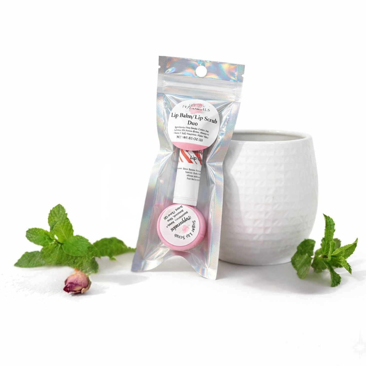 Lip balm and lip scrub duo in a clear packaging with a white container and mint leaves on a white background