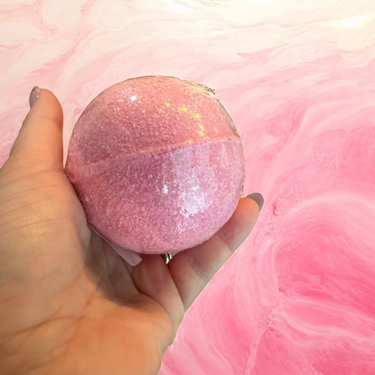 Hand holding a pink glitter bath bomb made with the Bubbly Botanicals recipe