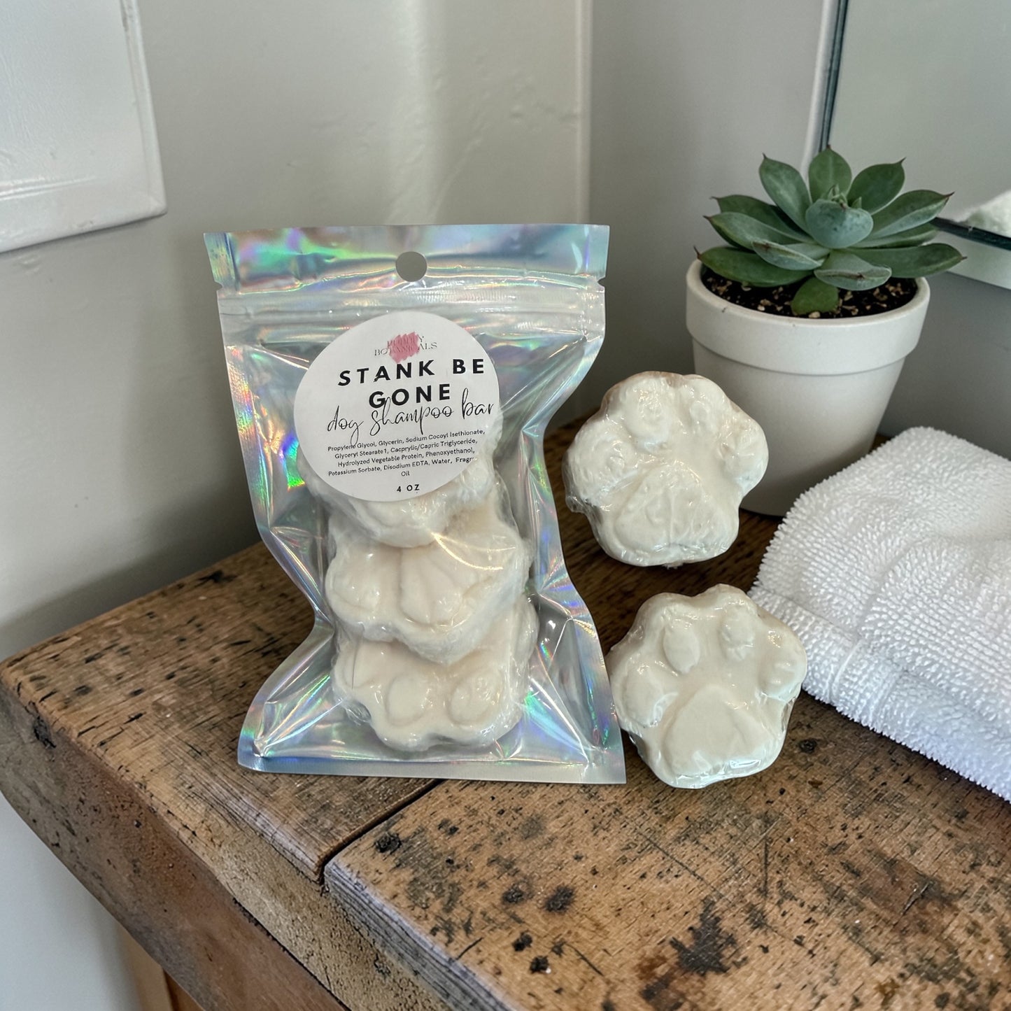 Packaged product labeled 'Stank Be Gone' on a wooden surface with a plant and towel in the background.