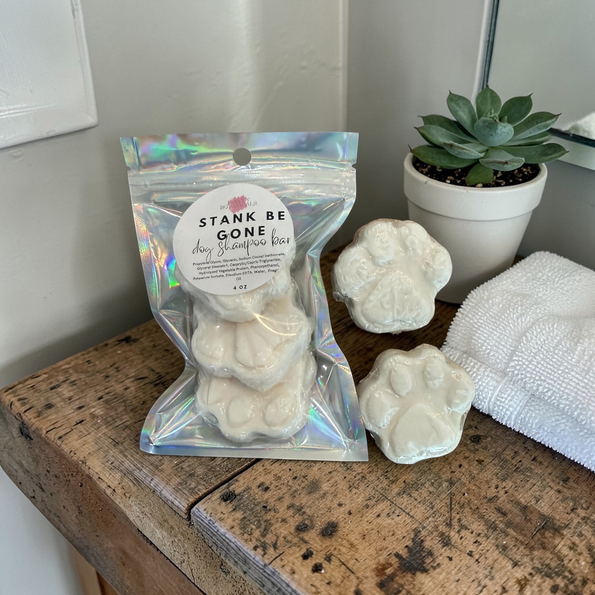 Packaged product labeled 'Stank Be Gone' on a wooden surface with a plant and towel in the background.