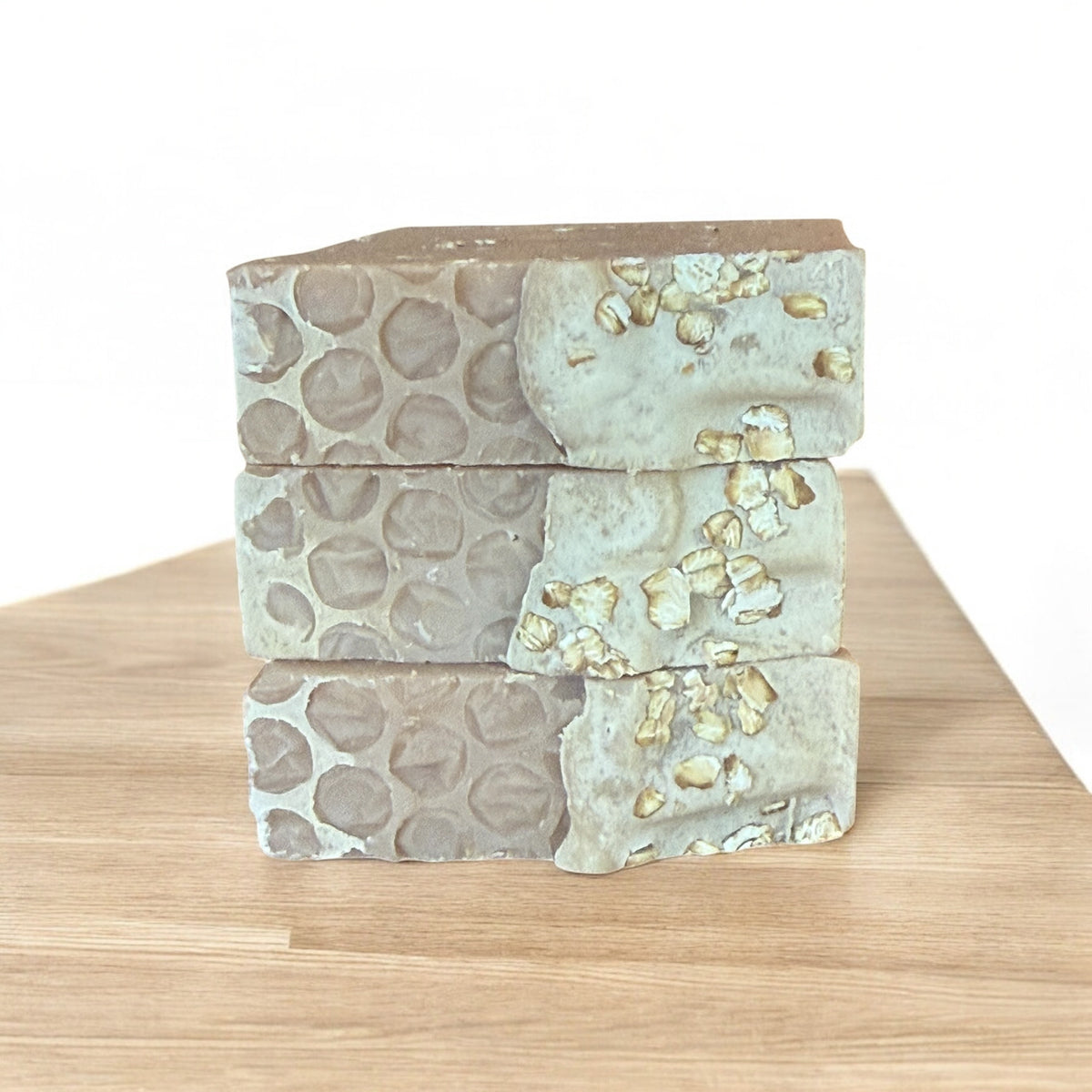 Three Sweet Honey & Oats tallow soaps by Bubbly Botanicals stacked on a wooden surface