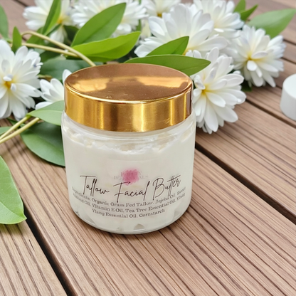 Jar of Tallow Facial Butter with a gold lid on a wooden surface with white flowers and green leaves.