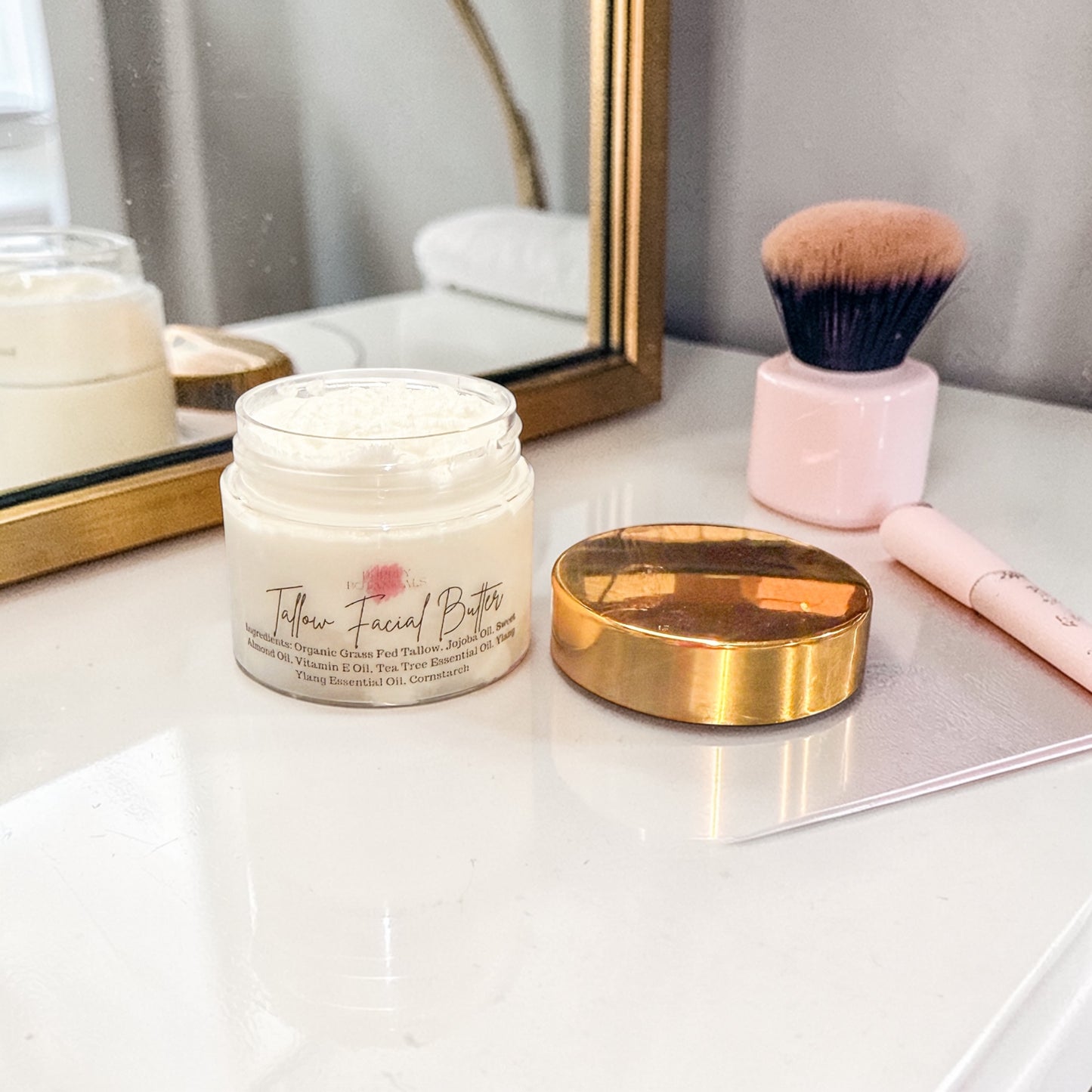 Jar of Tallow Facial Butter on a vanity with makeup brush and mirror.