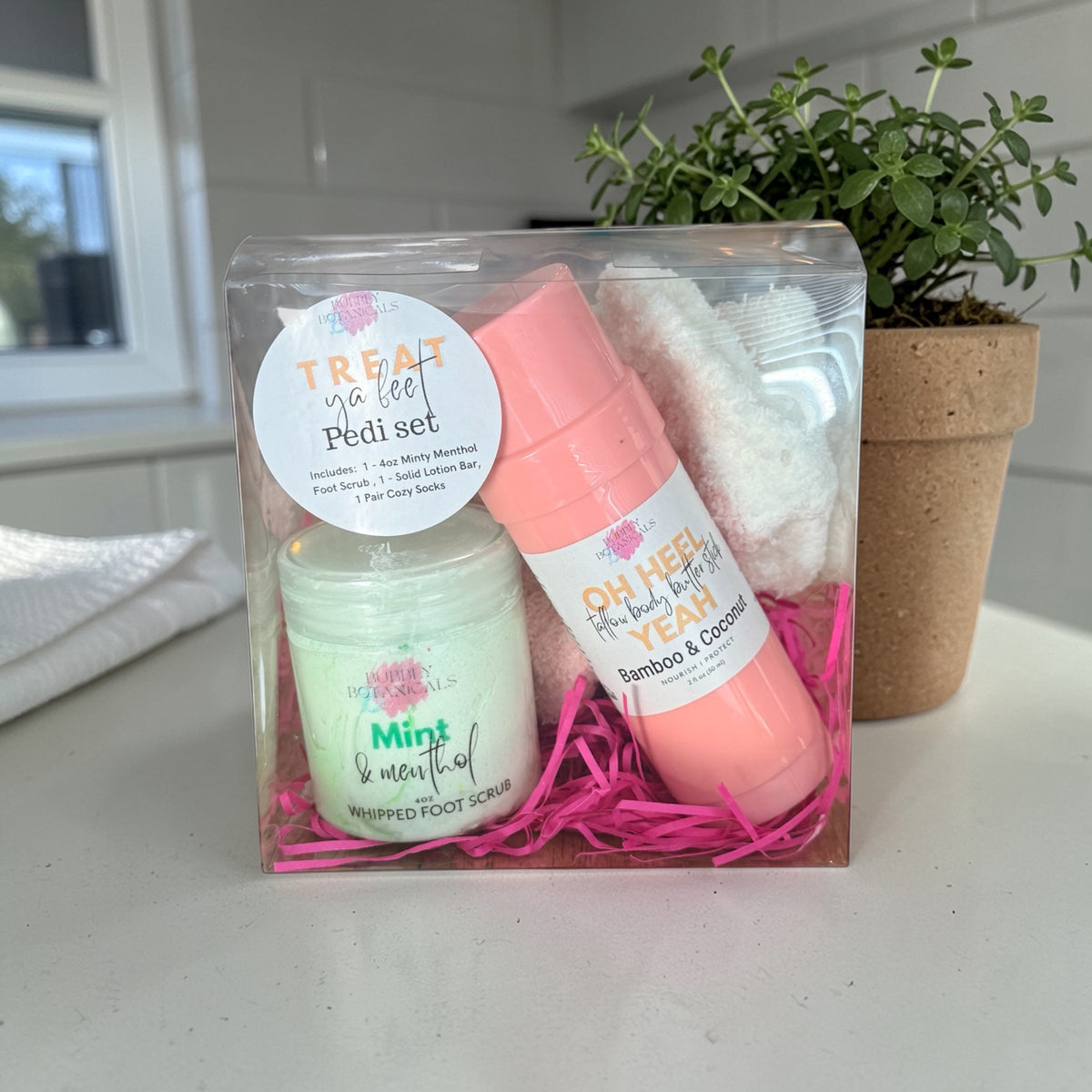 Treat ya feet pedi set with two products in a clear box on a white surface with a plant in the background.