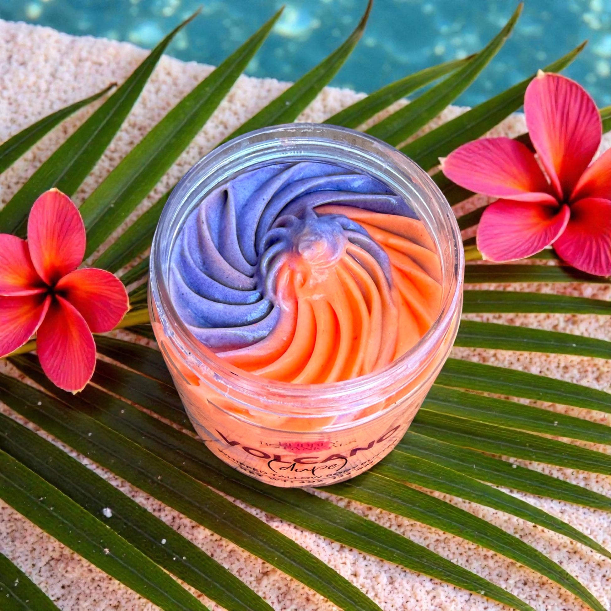 Colorful swirled Volcano tallow body butter in a jar with flowers and palm leaves on sand