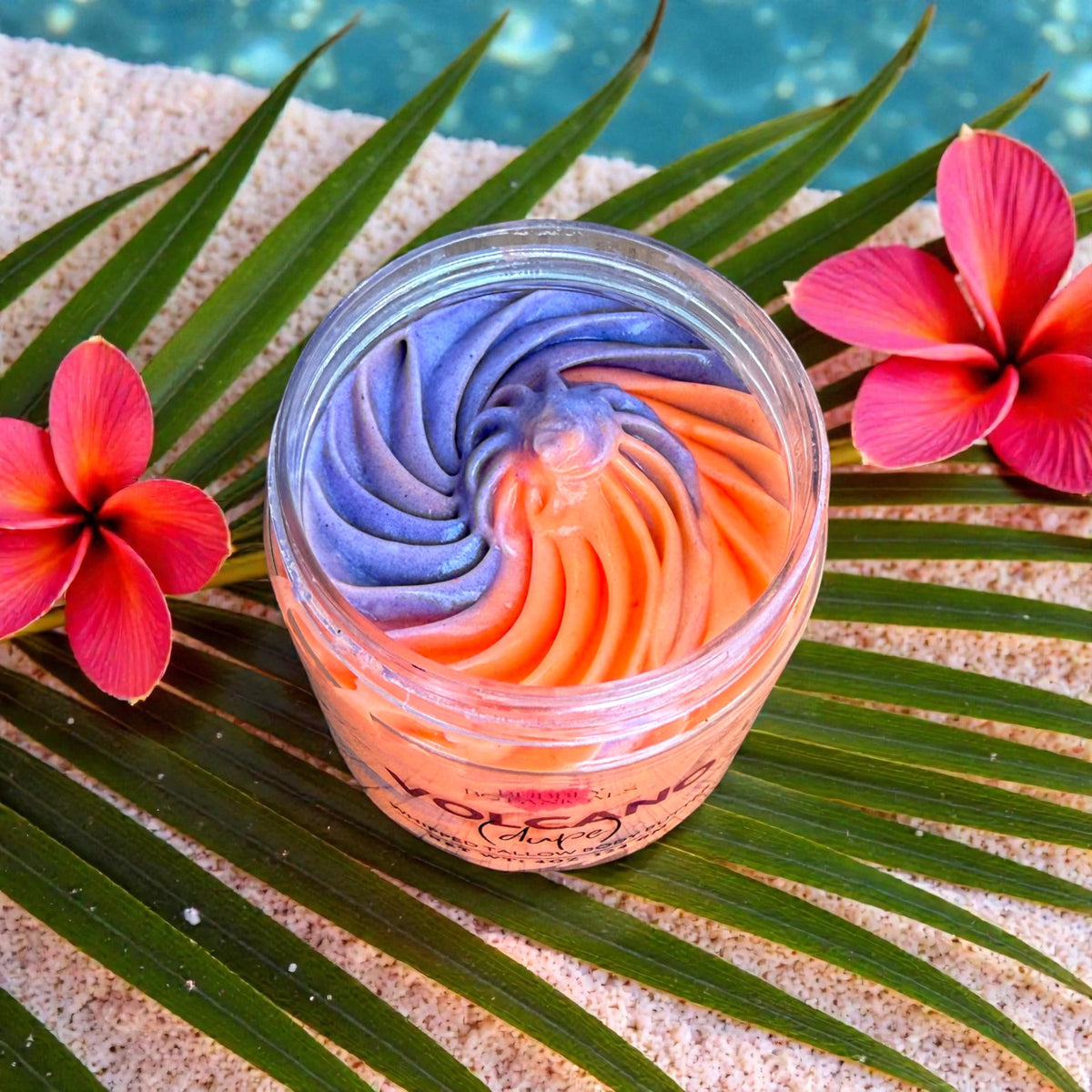 Colorful swirled Volcano tallow body butter in a jar with flowers and palm leaves on sand